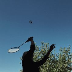 a person throwing a frisbee in the air with trees behind them and a bird flying overhead