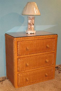 a lamp on top of a wicker dresser next to a blue wall and carpet