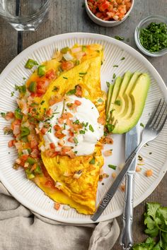 an omelet on a white plate with avocado and salsa next to it