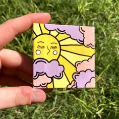 a hand holding up a small piece of paper with a sun and clouds on it