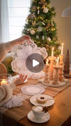 a woman is decorating a table with candles and plates in front of a christmas tree