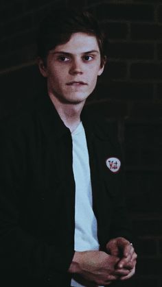 a young man in a black jacket and white shirt is posing for a photo against a brick wall