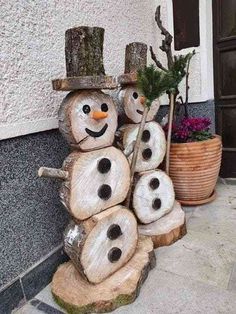 snowmen made out of logs sitting on the side of a building next to a potted plant