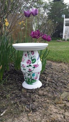 a white vase with flowers painted on it sitting in the grass next to some plants