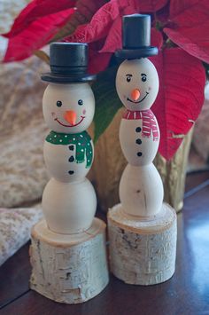 two snowmen are standing on logs with red poinsettia in the background