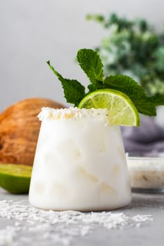 a coconut drink garnished with lime and mint on a white plate next to some other food