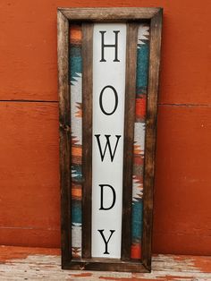 a sign that says howdy on it in front of an orange wall with a wooden frame