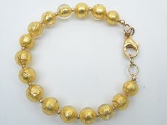 a gold beaded bracelet on a white surface with an oval clasp and round beads