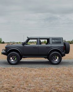 a black truck parked on the side of a road in front of a dry grass field