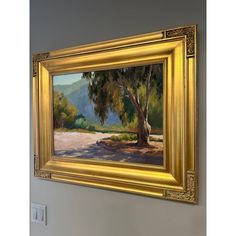 an oil painting of a tree in a golden frame hanging on the wall next to a light switch