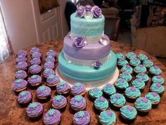 a cake and cupcakes on a table with purple and blue frosted icing