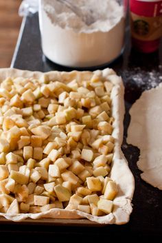 an uncooked apple pie sitting on top of a wooden table next to flour