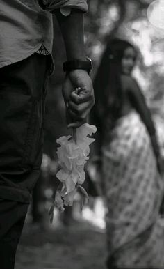 black and white photograph of two people holding hands with flowers in the foreground,