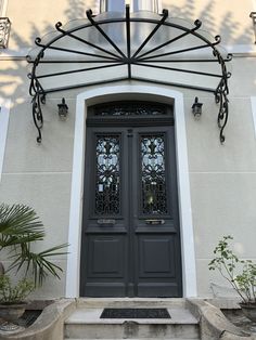 the front door of a house with two large doors and an iron trellis over it