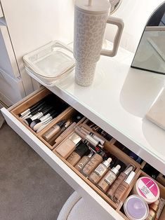 an open drawer with cosmetics and a coffee cup on the counter in front of it