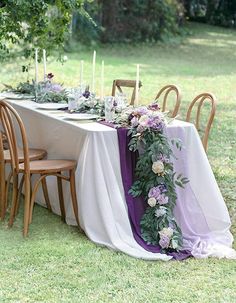 the table is set with purple flowers and greenery on it, along with candles