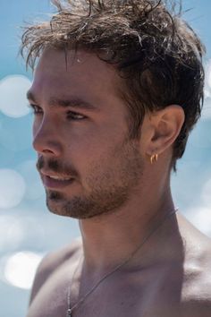 a man with no shirt on standing next to the ocean and looking off into the distance