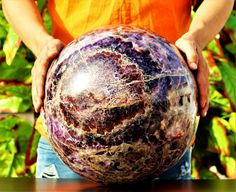 a person holding a large marble ball on top of a wooden table in front of some plants