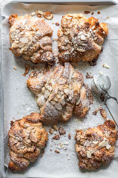 four pastries on a baking sheet covered in powdered sugar and topped with nuts