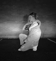 a woman sitting on the ground in front of a brick wall with her arms around her neck