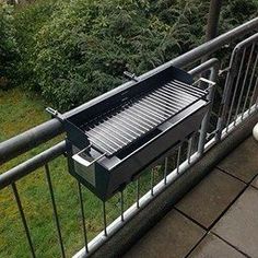 an outdoor grill on the side of a building with grass and bushes in the background