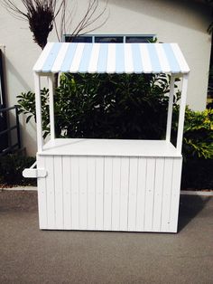 a white and blue striped awning on the side of a building next to bushes