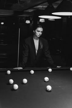 a black and white photo of a woman leaning over a pool table with balls in front of her