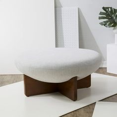 a white ottoman sitting on top of a wooden floor next to a potted plant