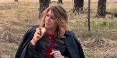 a woman is standing in the woods eating something out of her hand and looking off into the distance