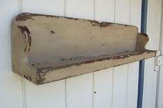 an old rusted metal shelf on the side of a building with white siding and blue pipe