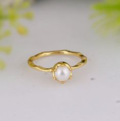 a gold ring with a white pearl in the middle and a green plant behind it