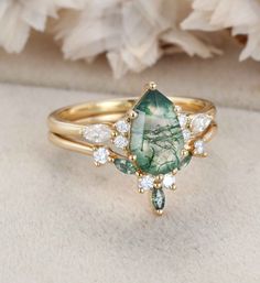 a green and white stone ring sitting on top of a piece of cloth next to flowers