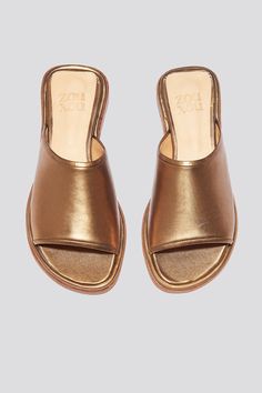 The Pileta slide is a streamlined version of the Pileta Sport Slide, featuring a sleek leather sole. The absence of details creates the perfect canvas for metallic bronze kidskin to shine. Slipping into a simple flat sandal in a striking material can be the answer to "dressing up" on a summer night when paired with a long strappy dress. Who it’s for: The woman who likes being the most comfortable person at the party.Kidskin upper with vegetable tanned leather lining and a 25 mm stacked leather h Gold Leather Slides With Leather Footbed, Classic Gold Sandals With Leather Footbed, Gold Leather Sandals With Rubber Sole, Gold Mules With Leather Sole For Summer, Gold Leather Open Toe Slides, Gold Open Toe Leather Slides, Classic Gold Sandals For Summer, Sleek Gold Leather Sandals, Sleek Metallic Sandals For Summer