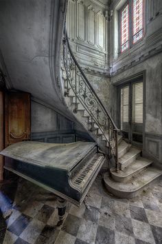 an old piano sitting in the middle of a room next to a stair case and door