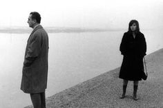 a woman standing next to a man near the water