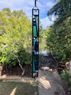 a stained glass sun catcher hanging from a chain in front of some trees and water