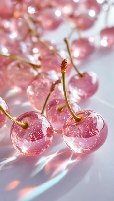 some pink cherries are lined up on a white tablecloth with shiny glass beads