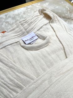 a white sweater with a label on it is sitting on a gold frame in a display case