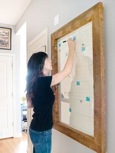 a woman standing in front of a wooden frame holding a white board with sticky notes on it