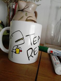 a white coffee mug sitting on top of a wooden table next to two batteries and a vase