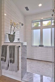 a white tiled bathroom with two towels hanging on the wall and flowers in a vase