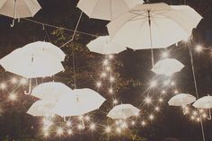 several white umbrellas hanging from strings with lights