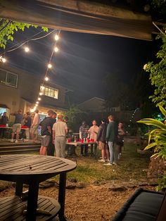 a group of people standing around in the yard at night with string lights strung over them