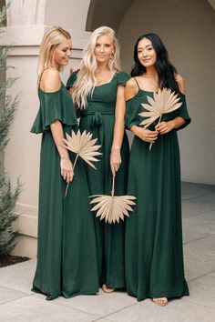 three women in green dresses standing next to each other with palm leaves on their backs