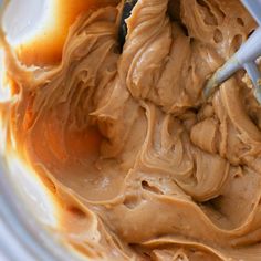 a bowl filled with peanut butter and caramel colored icing next to a spoon