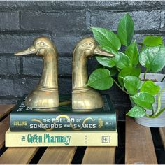 two golden ducks on top of some books and a potted plant next to them