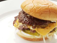 a cheeseburger with pickles and onions on a white plate