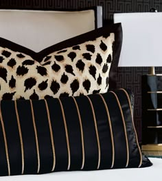 two black and gold pillows sitting on top of a white bed next to a lamp