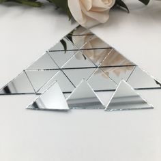 a white rose is sitting next to a triangle shaped mirror