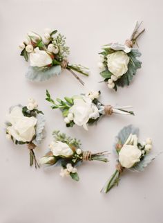 six boutonnieres with white flowers and greenery on the top are laid out